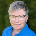 Lächelnde Dame mit leicht grau-melierten Haaren und einer runden Brille